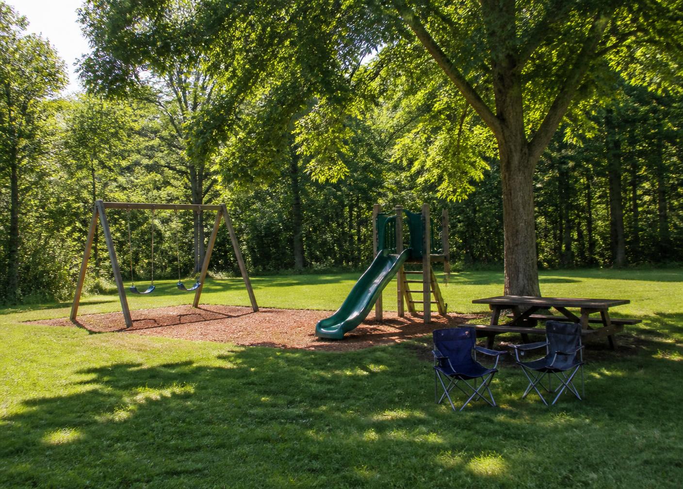 Shaded playground with swings and a slide beside the sites